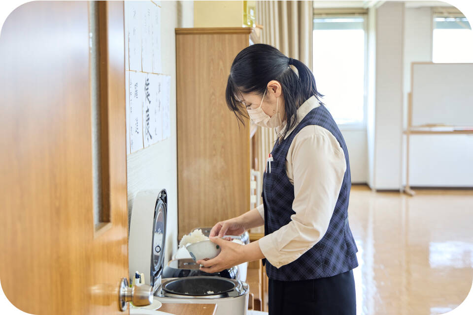 炊飯器からお椀にご飯を分けている女性の画像